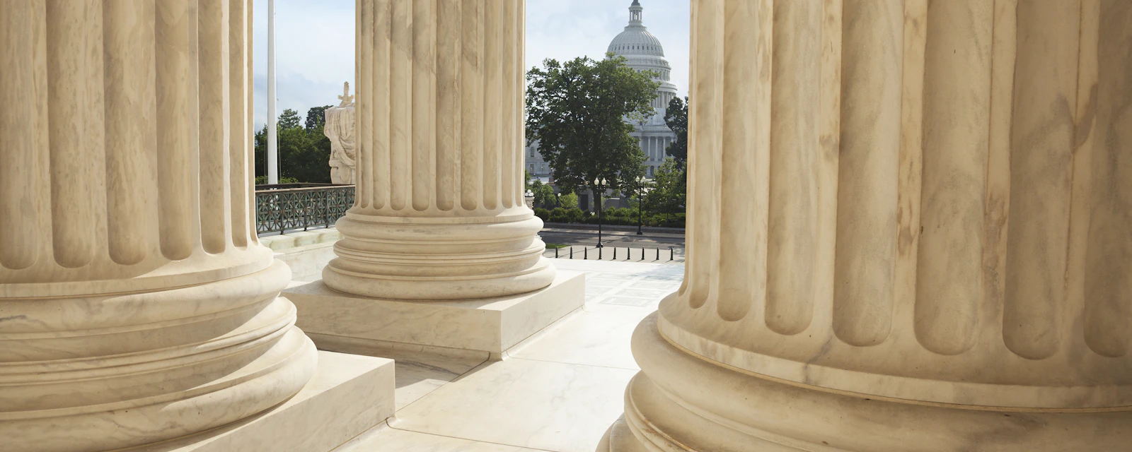 Close up of the columns of the Supreme Court building with an American flag and the US Capitol in the background